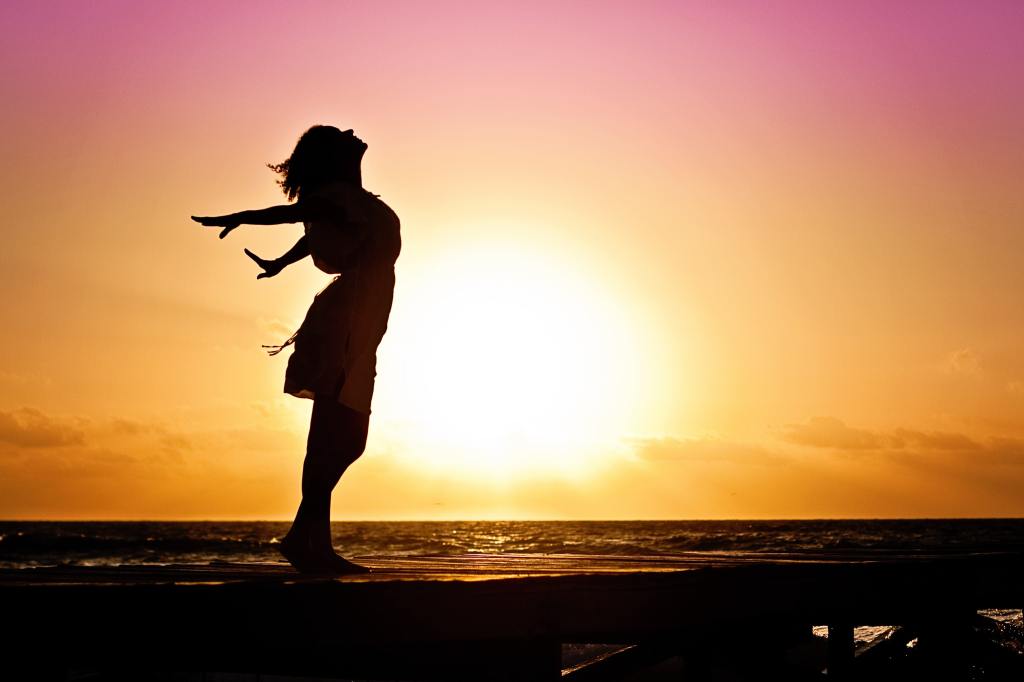 woman opening her arms wide in freedom with the sun shining