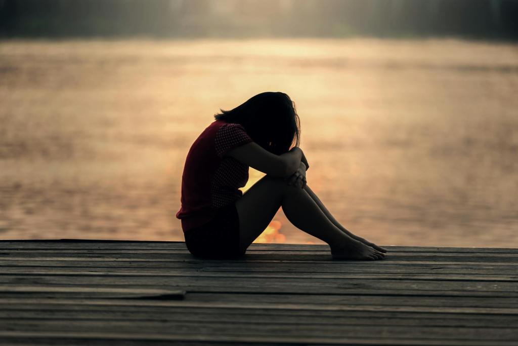 Woman by herself on a pier by the sea with head buried in knees