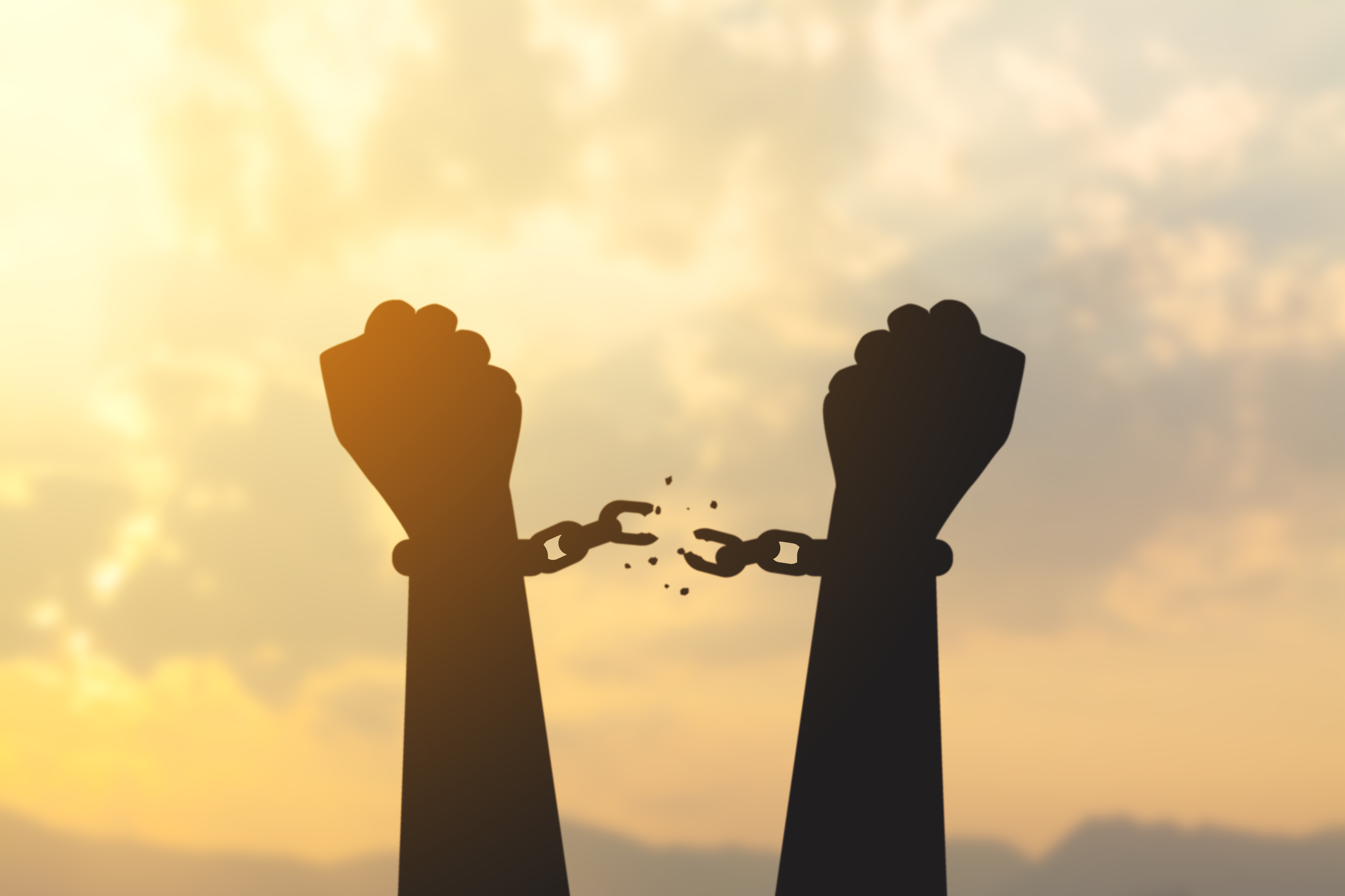 silhouette of two fists in air with chains breaking off hands with sun in the background